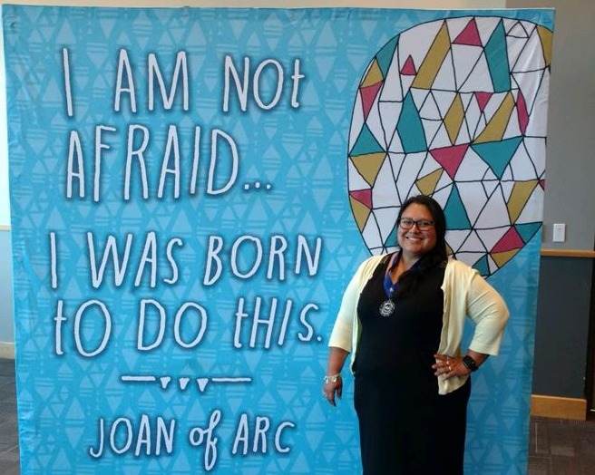 Teacher stands in front of Joan of Arc quote at a Star Educator ceremony.